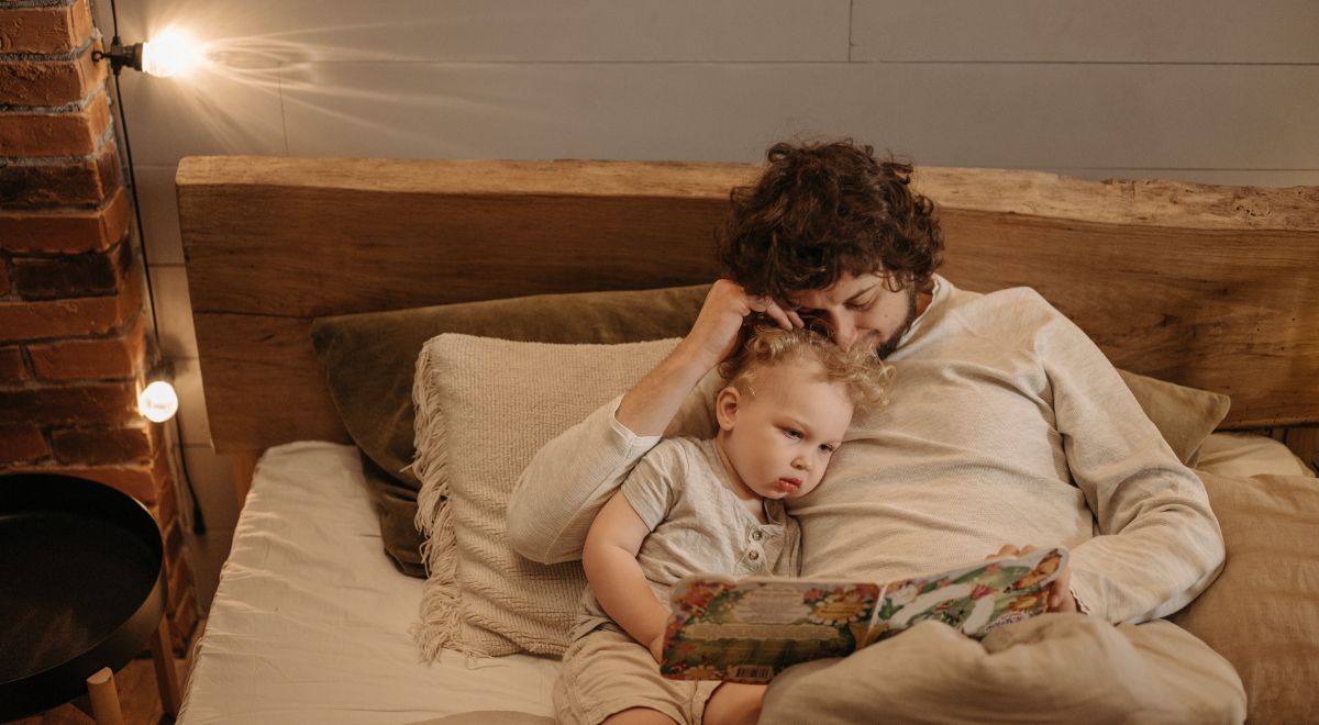 Mãe e filha encostadas na cabeceira da cama lendo uma história bíblica infantil